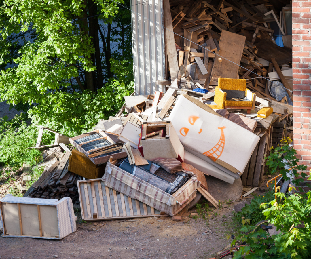 Pile of discarded furniture, wood, and debris stacked beside a garden building